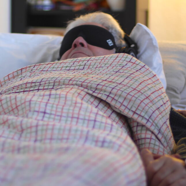 During a MDMA therapy session, a person is wrapped in a blanket and lays on a couch with blindfolds on — coverage from STAT