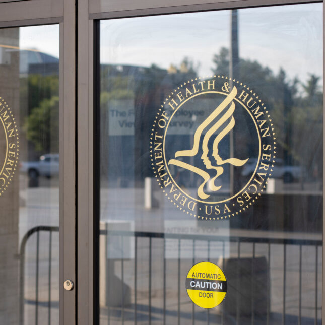 Both parts of an automatic door is decorated with a golden decal seal of U.S. Department of Health and Human Services — health tech coverage from STAT