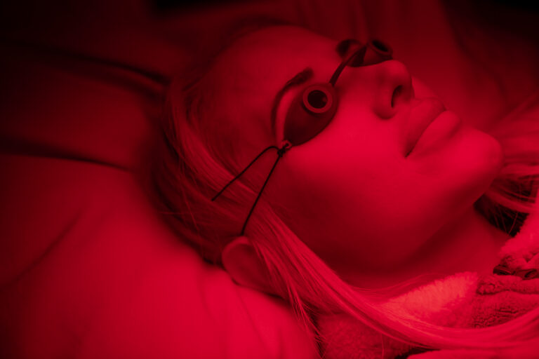 A close up photograph of Almas Eftekhari in a red light therapy chamber that she uses to try to treat symptoms from her chronic diseases