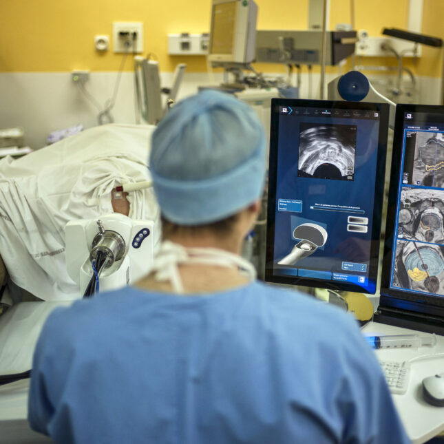 A surgeon sitting in front of screens of a Focal Onedevice performs a robot-assisted prostate tumorectomy using ultrasound imaging