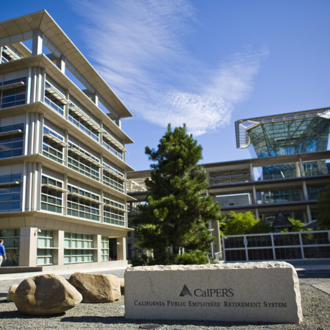 The text "CalPERS" and "California Public Employees’ Retirement System" engraved on a stone sign in front of an L-shaped glass building — business coverage from STAT