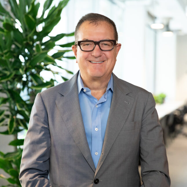 Portrait of a man with short brown hair and glasses poses for a portrait. He's waering a baby blue button down shirt and a grey blazer. -- biotech coverage from STAT