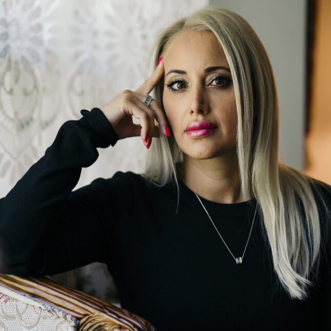 A portrait of Almas Eftekhari in her home wearing a black sweater and sitting next to a window. Eftekhari, a 40-year-old Lyme disease advocate, shrugged off her first, super-mild bout of Covid in August of 2023