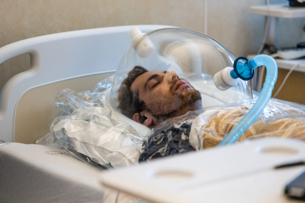 Joel Landy, 28, a participant in a study on the effects of ultra-processed diets, has his resting energy expenditure measured on Aug. 14, 2024, in his room at the National Institutes of Health in Bethesda, Maryland. During the 45-minute assessment, Landy rests in bed with his head in a ventilated hood but cannot fall asleep. Led by Principal Investigator Kevin Hall, the study compares participants' energy metabolism in response to ultra-processed versus unprocessed foods.